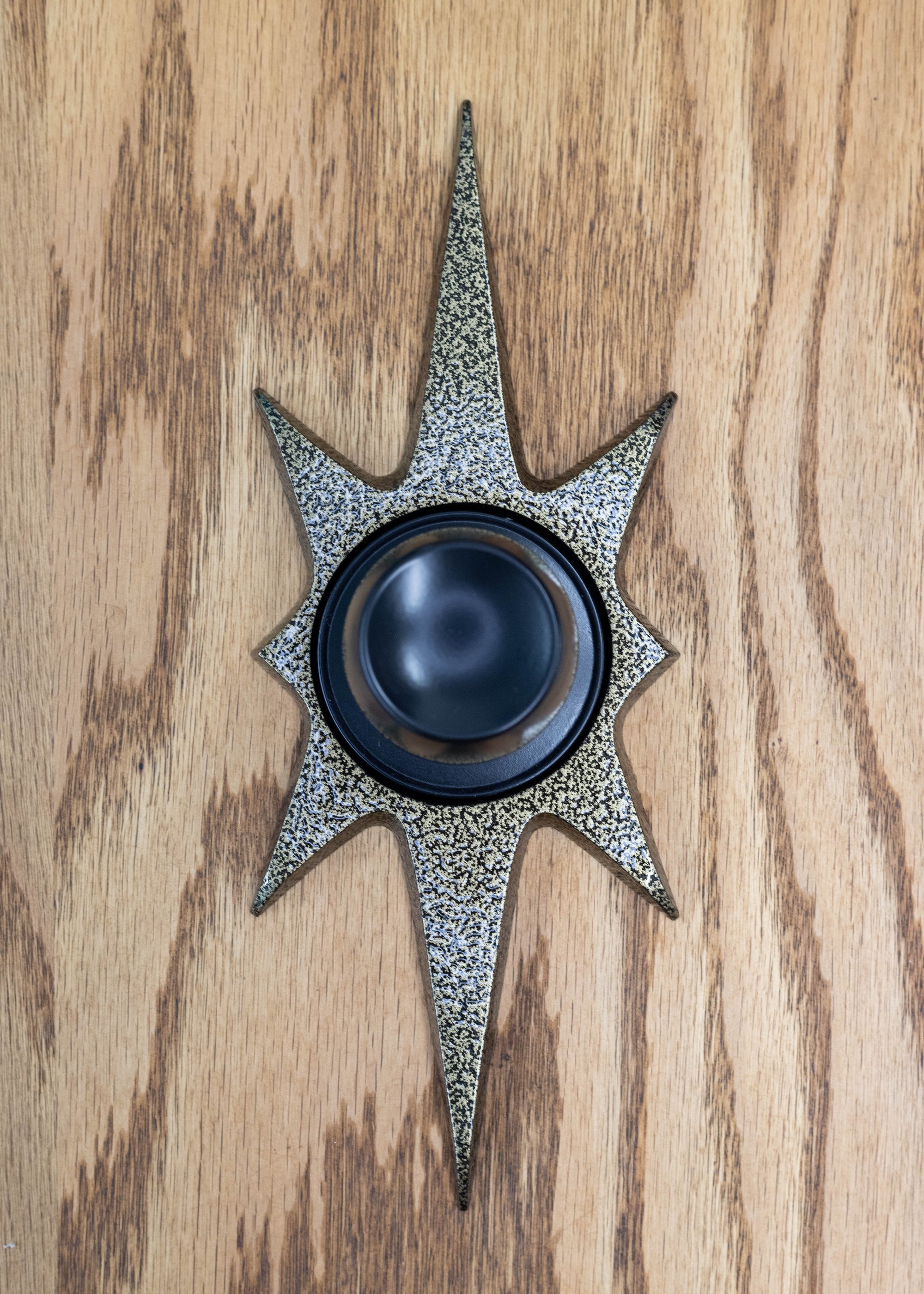 Gold vein starburst doorknob escutcheon.  The gold vein powder coating has a crackled texture that is a mixture of gold and black. It is still smooth and glossy, giving reflection to light. It is paired with a black knob in this photo.