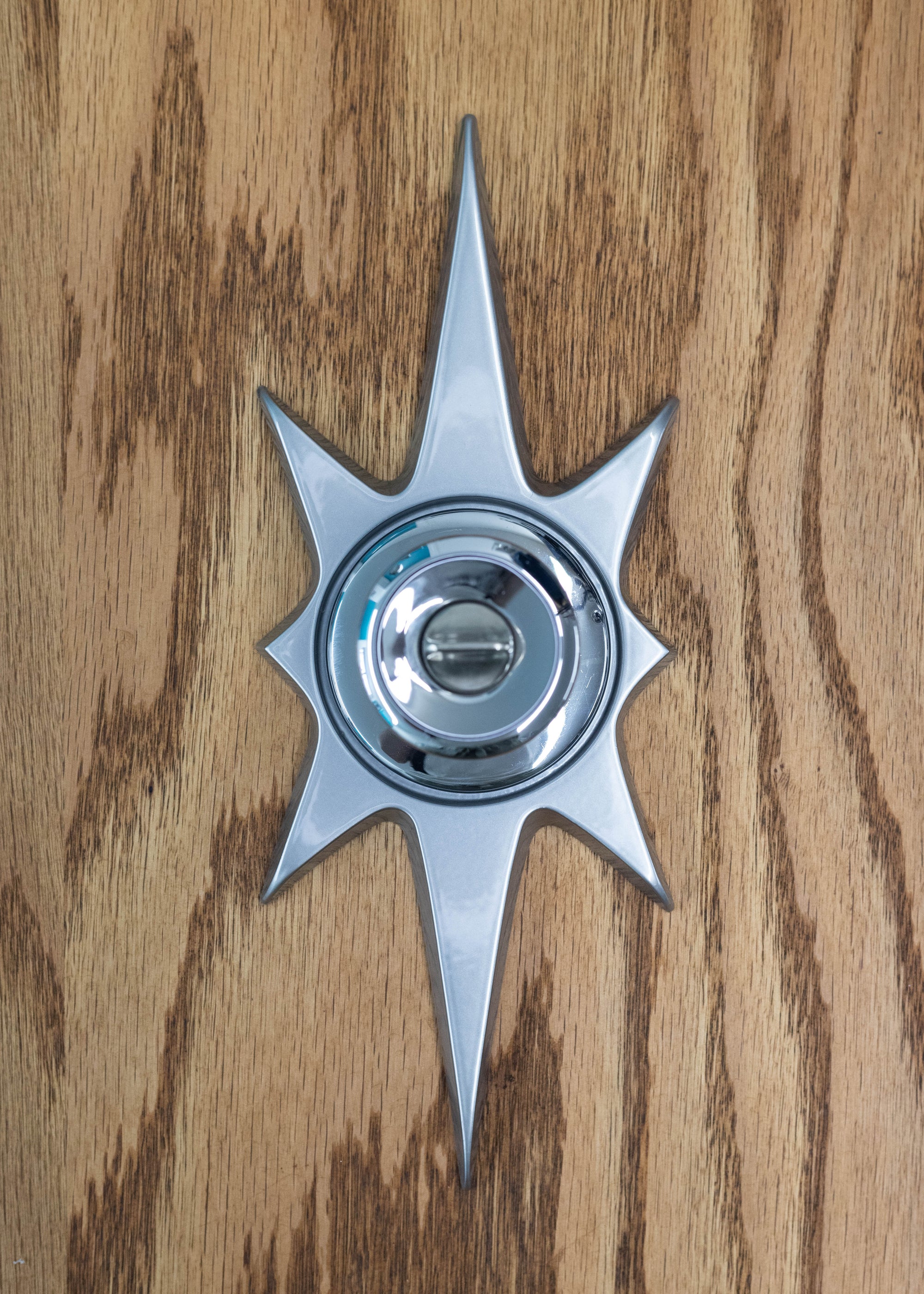 A silver starburst doorknob escutcheon paired with a silver door knob (knob not for sale). It is silver powder coated which gives it a very glossy and smooth finish.The starburst consists of two long points on top and bottom, 2 very short points horizontal, and 4 medium points diagonal.