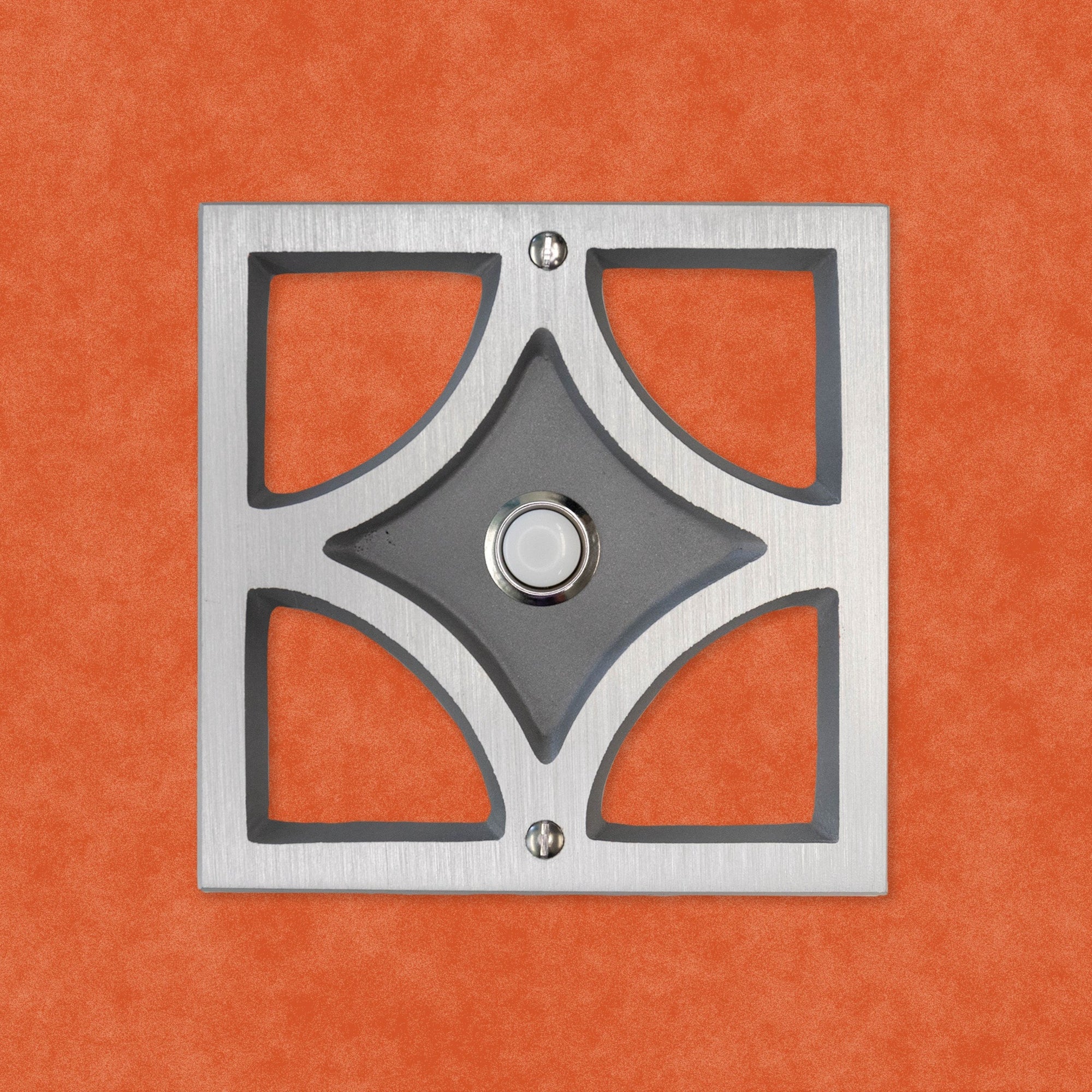A natural cast aluminum breeze block with a silver rimmed door bell button and screws. The breeze block design is a square exterior with a diamond shape inside, leaving 4 hollow corners. The middle of the diamond is sunken in, and that is where the doorbell button is. On the inner areas and sunken middle diamond, it is natural cast aluminum, while the face is brushed aluminum to give it a brighter contrast.