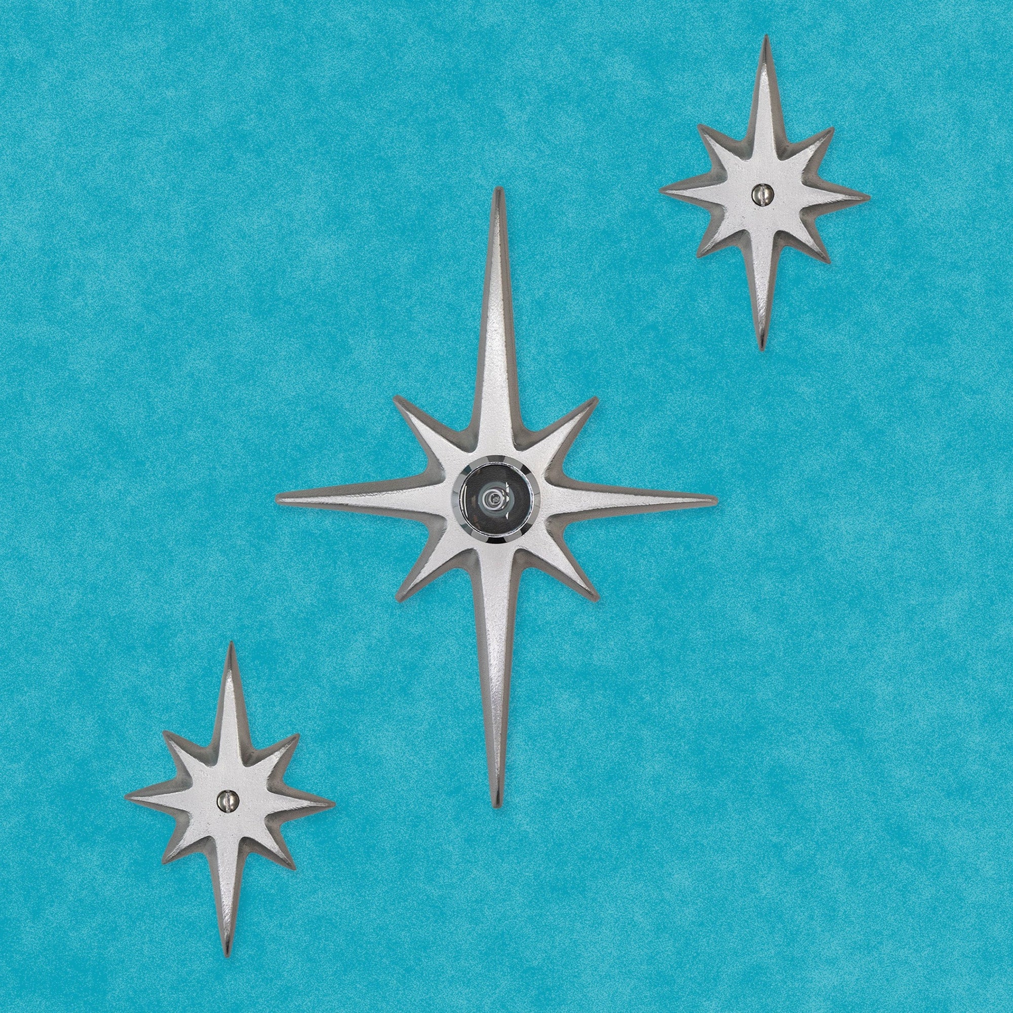 set of 3 cast aluminum starbursts with a peephole viewer. The peephole viewer is in the center of a medium 7.5 inch tall starburst. The other two are small starbursts each with a screw in their center.. They're all natural cast aluminum, so they are a light silver in color and while smooth to touch, have a slightly porous surface to them.