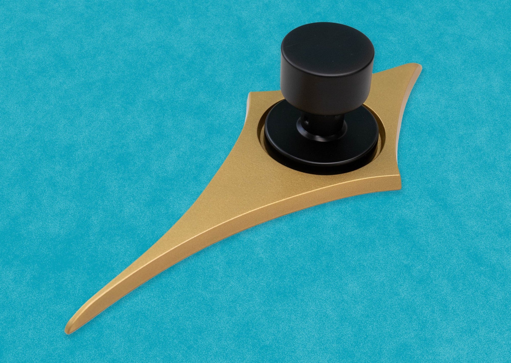 Angled view of the gold comet with a black doorknob. You can more easily see how smooth and flat the face of the escutcheon is, but the top and bottom points are rounded over the edge. The two shortest points horizontally remain flat.