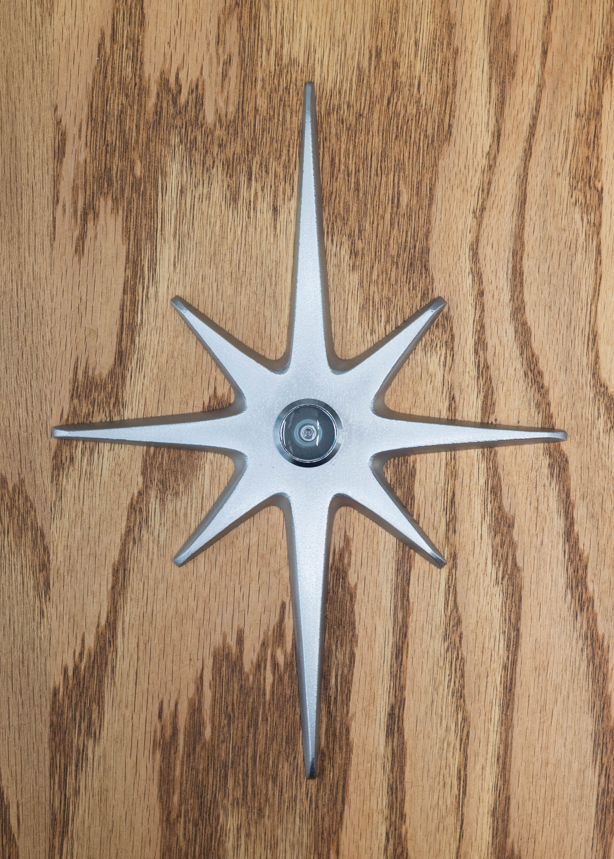 A large cast aluminum starburst with a peephole at the center. This one is natural aluminum with a silver peephole. The natural aluminum is a light silver in color, has a very slight porous texture to it, but is still smooth and gives a matte reflection of light.