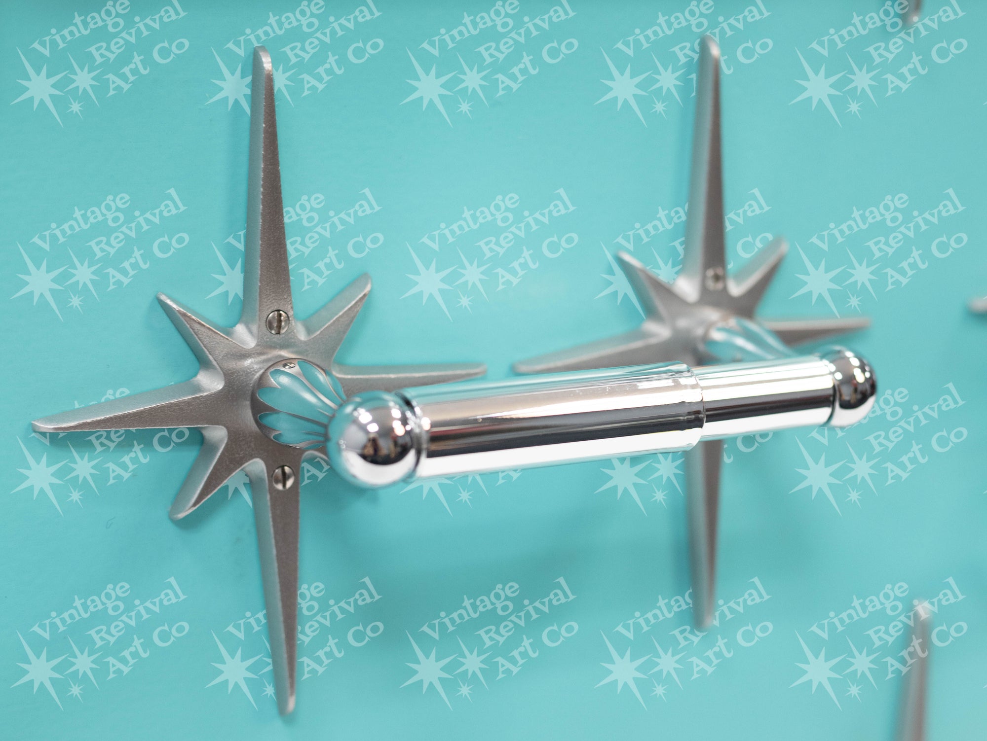 A standard toilet paper holder with two natural cast aluminum starbursts wear it attaches to the wall. They are silver with a metallic shine, and the hardware is chrome.