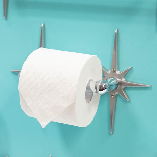 The toilet paper holder with a roll of toilet paper on it. You can see the starbursts sticking out from the sides and are only partially obscured by the full roll of toilet paper.