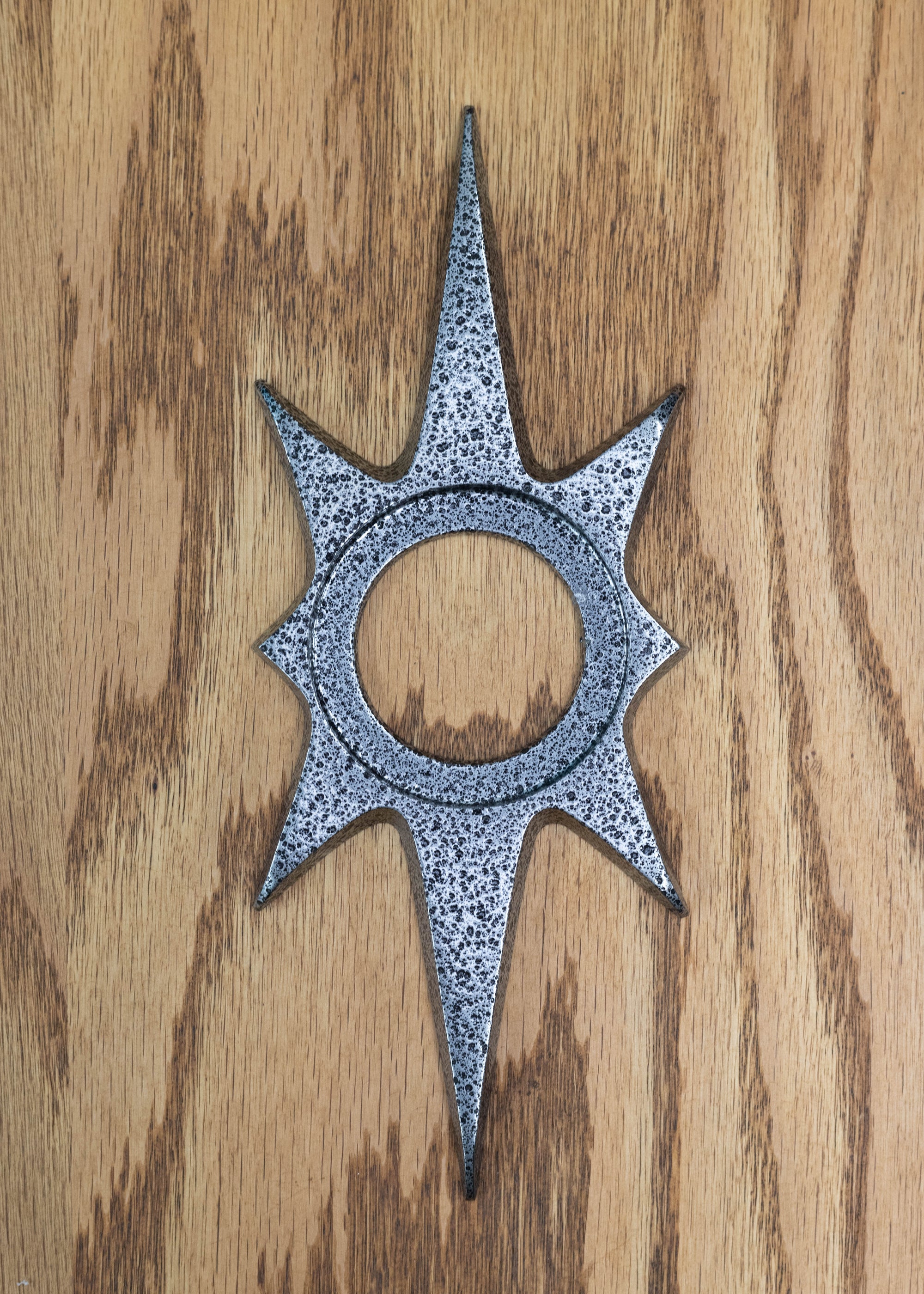 A starburst doorknob escutcheon (backing plate that goes behind.around your doorknob). There is an inset circle in the middle were the doorknob would sit into.It is a dark silver, almost gunmetal color with a porous/pitted texture that is black. The starburst consists of two long points on top and bottom, 2 very short points horizontal, and 4 medium points diagonal.