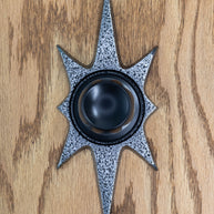 A starburst doorknob escutcheon with a black door knob. (knob not for sale) It is a dark silver, almost gunmetal color with a porous/pitted texture that is black. The starburst consists of two long points on top and bottom, 2 very short points horizontal, and 4 medium points diagonal.