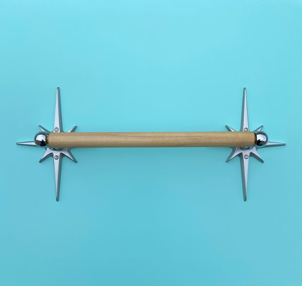 A silver paper towel holder with a mid-century modern atomic starburst design mounted on a blue wall.