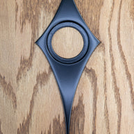 Matte black powder coated comet doorknob escutcheon. The surface is very smooth, and reflects light but is not glossy. The comet shape is like a diamond with slightly curved in edges and the bottom point is long. There is a hole in the center where the door knob goes.