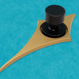 Angled view of the gold comet with a black doorknob. You can more easily see how smooth and flat the face of the escutcheon is, but the top and bottom points are rounded over the edge. The two shortest points horizontally remain flat.