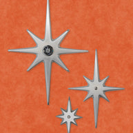 A set of three cast aluminum starbursts: Large, medium, and small. The largest one has a peephole viewer in the center, while the other two have a single screw at their centers. The style of starburst has the 2 longest points top and bottom, 2 medium points horizontal, and the other 4 shortest points diagonal in between. The aluminum is silver in color. They have a smooth but slightly textured finish due to the natural aluminum. There is slight shine, but are not glossy.