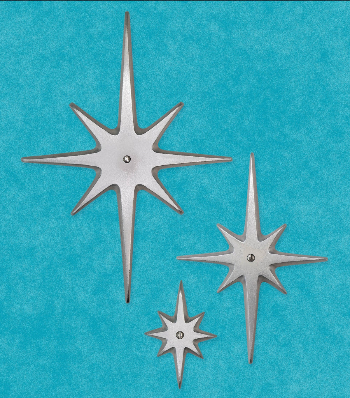 Three handcrafted aluminum Atomic Starbursts in graduated sizes with hammered finishes, arranged on a mid-century modern door.