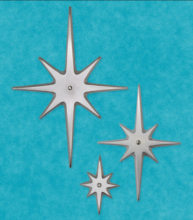 Three handcrafted aluminum Atomic Starbursts in graduated sizes with hammered finishes, arranged on a mid-century modern door.