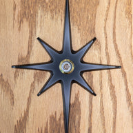 A large cast aluminum starburst with a peephole viewer in the center. The starburst has a black powder coating and the peephole is gold rimmed. The powder coat finish is matte, so it's not glossy with shine, but the surface is still smooth and gives slight reflection of light.
