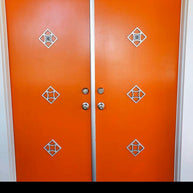 Double orange entry doors with breeze block peephole views and decorative plates