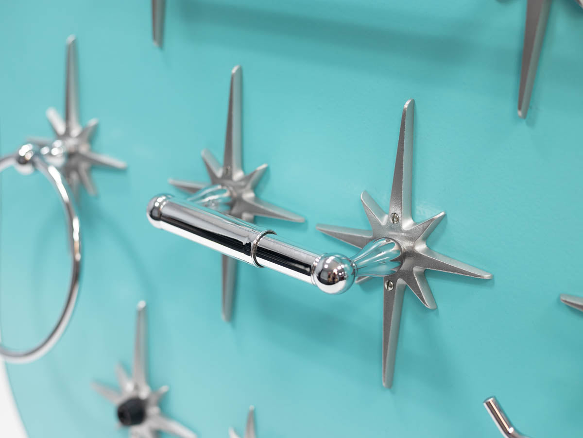 Mid-century modern toilet paper holder with chrome-finished spring rod.