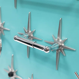 Mid-century modern toilet paper holder with chrome-finished spring rod.