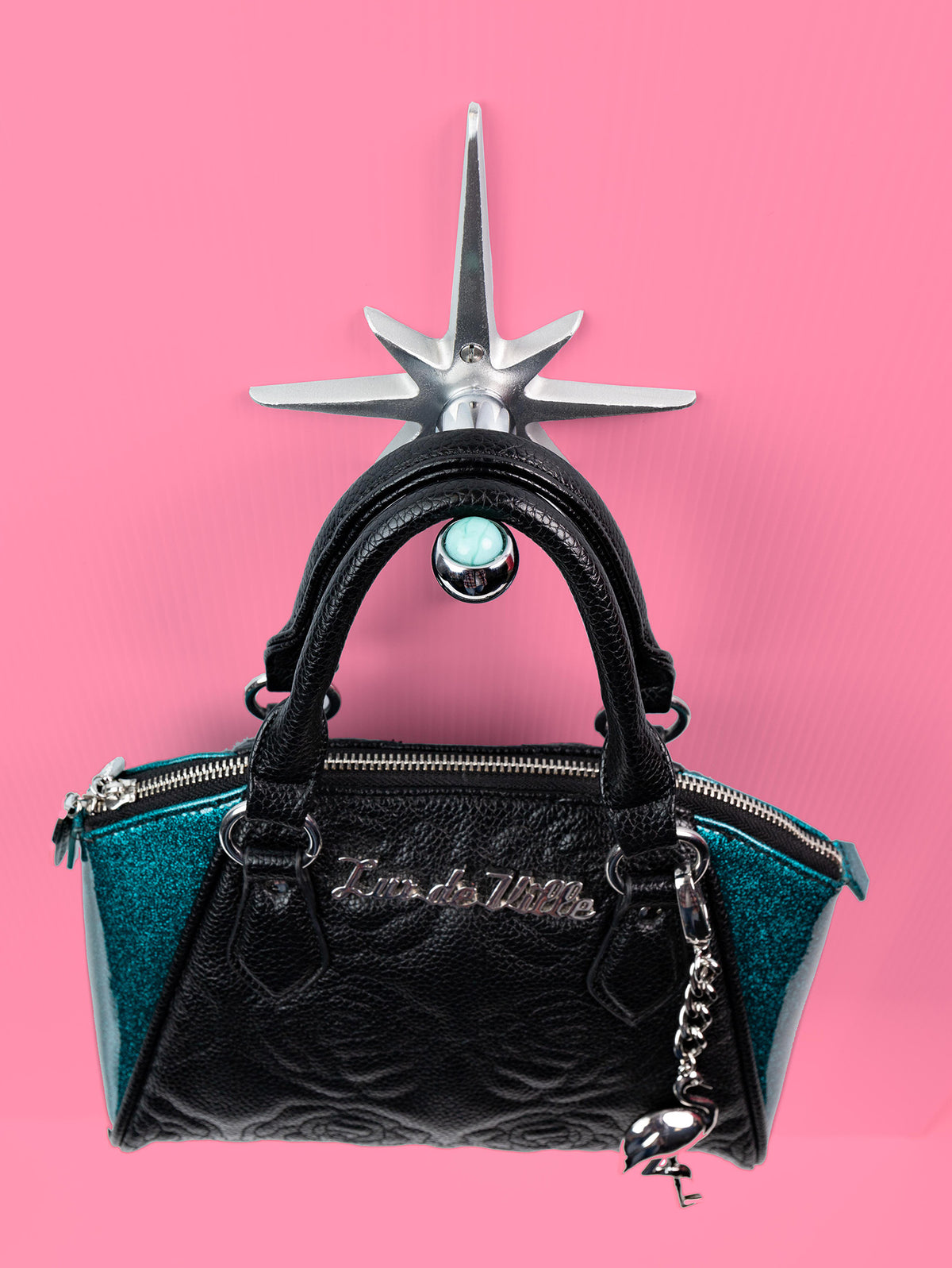A handcrafted cast aluminum starburst purse/coat hanger with a marble design, displayed against a pink background with a black purse hanging from it.