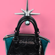 A handcrafted cast aluminum starburst purse/coat hanger with a marble design, displayed against a pink background with a black purse hanging from it.