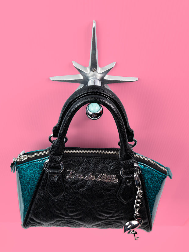 A handcrafted cast aluminum starburst purse/coat hanger with a marble design, displayed against a pink background with a black purse hanging from it.
