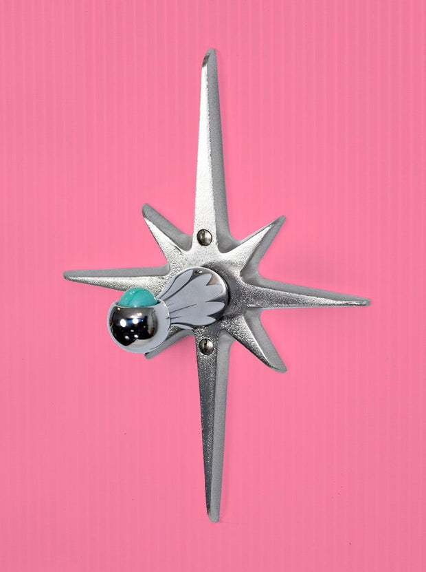 Closer view of the starburst purse/ coat hanger. The base that attaches to the wall is a cast aluminum starburst that is silver in color. Has naturally slightly porous surface texture, but is still very smooth and has a metallic shine to it. The hook part is chrome, and has a ball at the end that holds a marble.